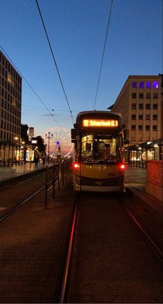 a city bus driving down the street at night with its lights on and buildings in the background