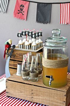 a party with cupcakes and drinks on a wooden crate in front of a pirate flag banner