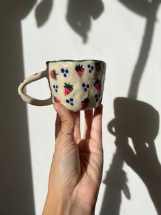 a hand holding a coffee cup with strawberries and blue berries painted on the inside