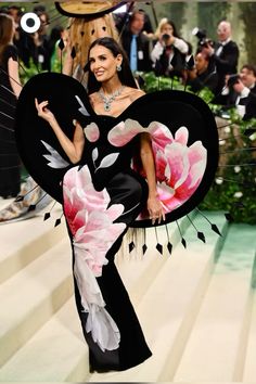 a woman in a black and white dress with pink flowers on her body, holding a fan