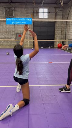 two girls are playing volleyball in an indoor gym with purple flooring and white walls