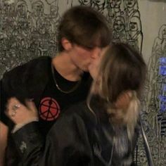 a man and woman kissing each other in front of a wall with graffiti on it