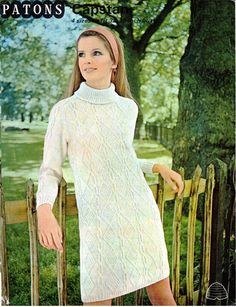 a woman in a white sweater dress standing next to a fence with her hands on her hips