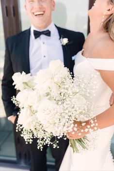 the bride and groom are standing outside together smiling at each other as they hold their bouquets