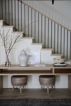 two stools sit in front of a table with vase on it and stairs leading up to the second floor