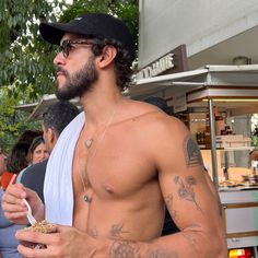 a man with no shirt eating food from a paper bag while standing in front of a group of people