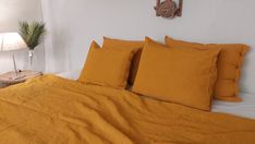 a bed with yellow linens and pillows in a white room next to a lamp