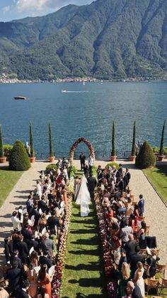 an outdoor wedding ceremony on the lawn by the water with mountains in the background and greenery