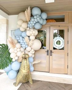 a balloon arch with blue, white and gold balloons on it in front of a house