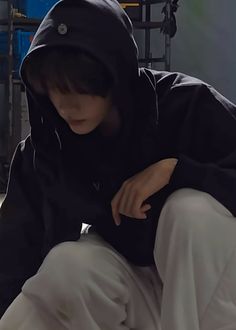 a person sitting on the ground wearing a black hoodie