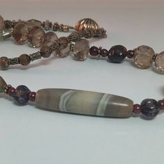 What an unusual combination of subtle colors and textures - starting off with the stunning off centered antique banded agate (it even has an eye to the beautifully faceted smoky quartz beads, to the various bronze tone beads, sterling spacers/box clasp and rich, rich burgundy garnets (raw tumbled and finished).  Perfect colors for this fall's fashion trends.  All over the world since ancient times, mankind has feared the 'evil eye' and used talismans or stone/glass beads to protect themselves. Elegant Hand-strung Agate Necklace, Artisan Necklace With Czech Glass And Natural Stones, Artisan Necklace With Natural Stones And Czech Glass, Artisan Czech Glass Necklaces With Natural Stones, Artisan Czech Glass Necklace With Natural Stones, Elegant Jasper Gemstone Jewelry, Elegant Handmade Jasper Necklaces, Elegant Handmade Jasper Necklace, Handmade Jasper Elegant Necklace