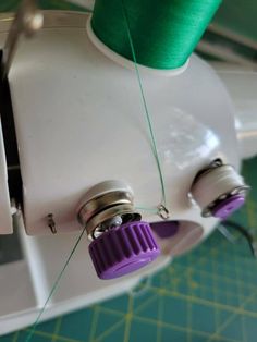 the sewing machine is being worked on with green thread and two purple spools