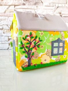 a small house made out of fabric with a tree on the front and side, sitting next to a brick wall