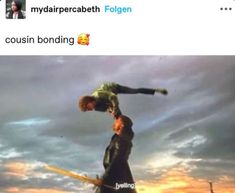 two people standing on top of each other in front of a sky with clouds and one person doing a handstand