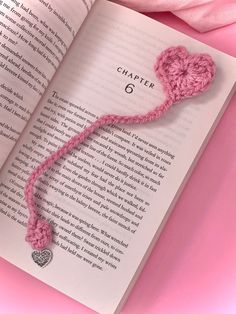 an open book with a pink crocheted heart on it and a string attached to the page