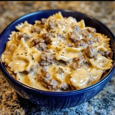 a blue bowl filled with pasta and meat covered in sauce on top of a granite counter