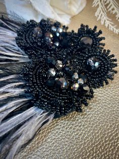 two pieces of black beaded broochies with feathers on a white fabric background