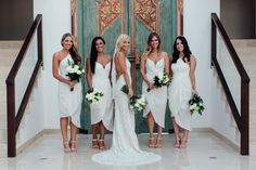 a group of women standing next to each other in front of a door wearing white dresses