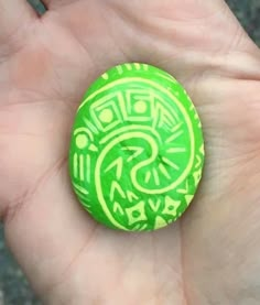 a hand holding a green and yellow painted rock