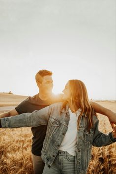 a man and woman standing in a wheat field holding each other's arms as the sun shines brightly behind them