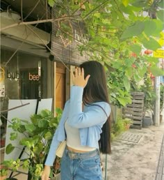 a woman standing in front of a tree talking on a cell phone while holding her hand up to her face