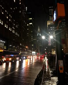 a city street filled with lots of traffic next to tall buildings at night in the rain