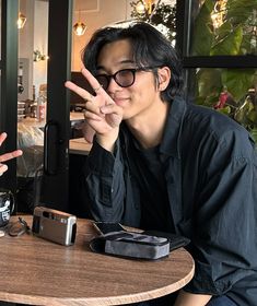 a man sitting at a table making the peace sign with his hands while holding a camera