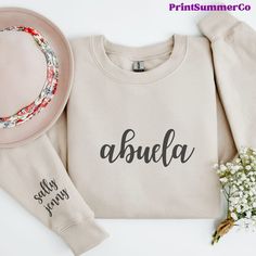 a sweater with the word abuella written on it next to a hat and flowers