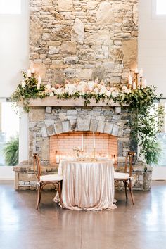 a table is set up in front of a fireplace with candles and flowers on it