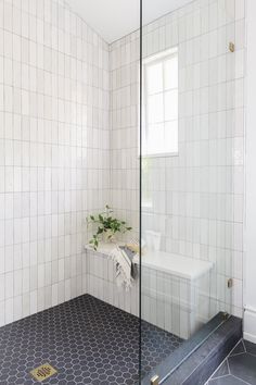 a bathroom with a glass shower door and tiled flooring, along with a plant in the corner