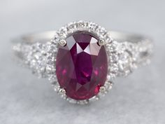 an oval shaped ruby and diamond ring with white gold accents, set on a gray surface