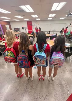 three girls with backpacks standing in a classroom