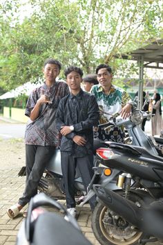 three men standing next to each other in front of motorcycles