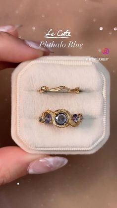 two gold rings with amethyst blue stones are in a white velvet ring box