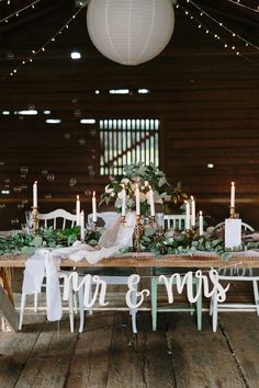 a wooden table topped with lots of white candles and greenery next to a sign that says mr and mrs