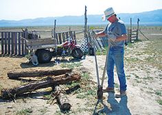 a man standing next to a pile of logs in the dirt near a wooden fence