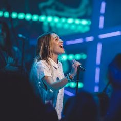 a woman singing into a microphone while standing in front of a crowd at a concert