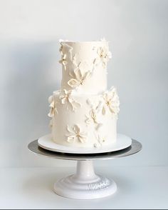 a three tiered white cake with flowers on it sitting on a silver platter