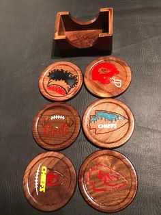 four wooden coasters with different sports logos on them and a rubber holder for magnets