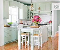 a kitchen with green cabinets and white counter tops, two stools at the island