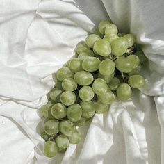 a bunch of green grapes laying on top of a white sheet covered in sheets and linens