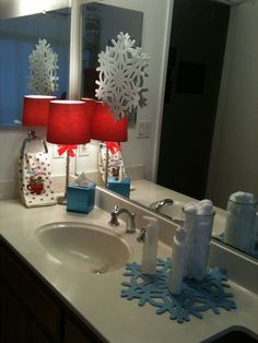 a bathroom sink with two red lamps on it's side and snowflakes hanging from the mirror