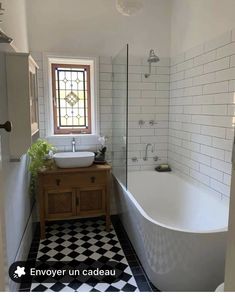 a white bath tub sitting next to a sink under a window in a bathroom with black and white tile flooring