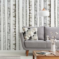 a living room with white birch trees on the wall and grey couch in front of it