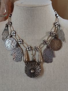 An assemblage of ethnic silver elements featuring a 925 sterling Yemeni amulet with the makers mark, possibly made by a Jewish Bawsani silversmith. I've flanked it with silver Turkmen pendulum shaped pendants, two walking liberty coin pendants from a Navajo squash blossom necklace, and Moroccan Berber Hamsa in two styles. All elements are suspended from triple plated silver chain. Finishes with a silver plated hook. Spiritual 925 Stamped Medallion Necklaces, Spiritual Medallion Necklace Stamped 925, Spiritual Medallion Necklaces Stamped 925, Vintage Sterling Silver Jewelry For Festivals, Artisan Engraved Jewelry For Ceremonial Occasions, Ceremonial Silver Medallion Necklace, Silver Medallion Necklace For Ceremonial Occasions, Silver Medallion Necklace For Ceremonial, Artisan Pendant Necklaces Stamped 925