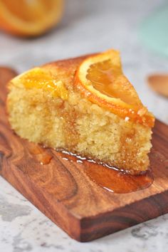 a piece of cake on a wooden cutting board with oranges in the back ground