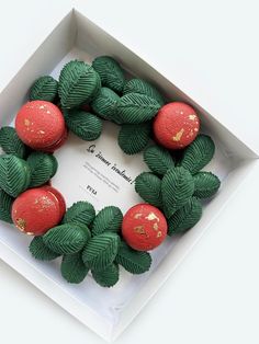 an open box with some green and red fruit in the shape of a wreath on top of it