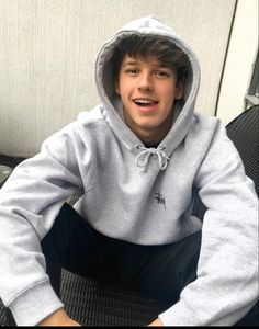 a young man sitting on top of a chair wearing a gray hoodie and black pants