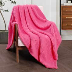 a pink blanket sitting on top of a white chair next to a potted plant