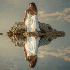 a woman sitting on top of a rock next to a body of water